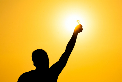 Man with light bulb against sunset sky